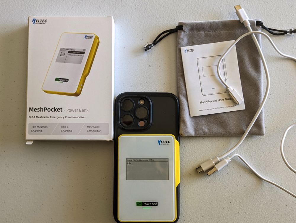 Image shows an iPhone attached magnetically to the Heltec MeshPocket and the contents of the package that are included in the MeshPocket's box including charging cable, data cable with pogo pins to communicate with Meshtastic device, and esp felt bag. 