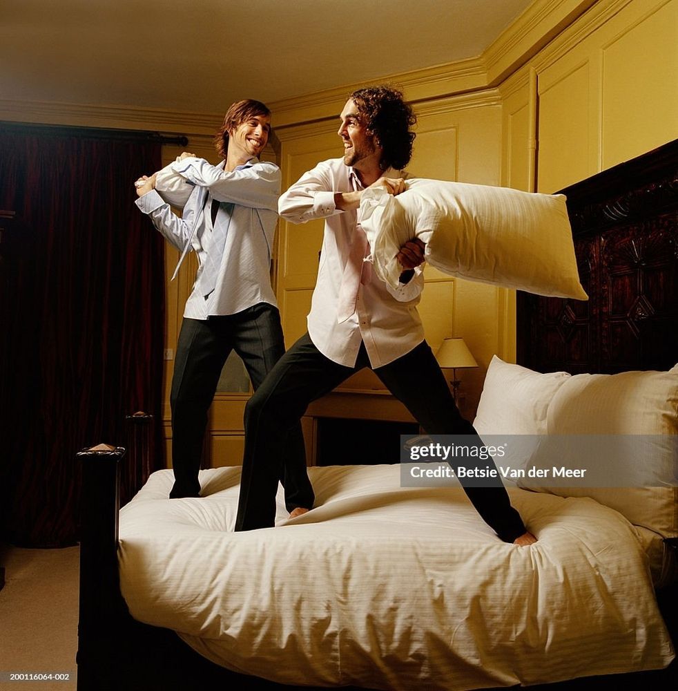 Two men pillow fighting on a bed