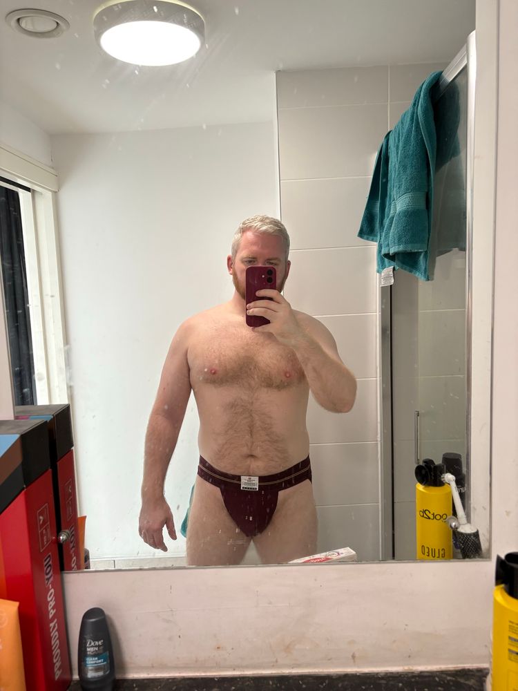 Me in a hookup’s bathroom in my maroon jockstrap