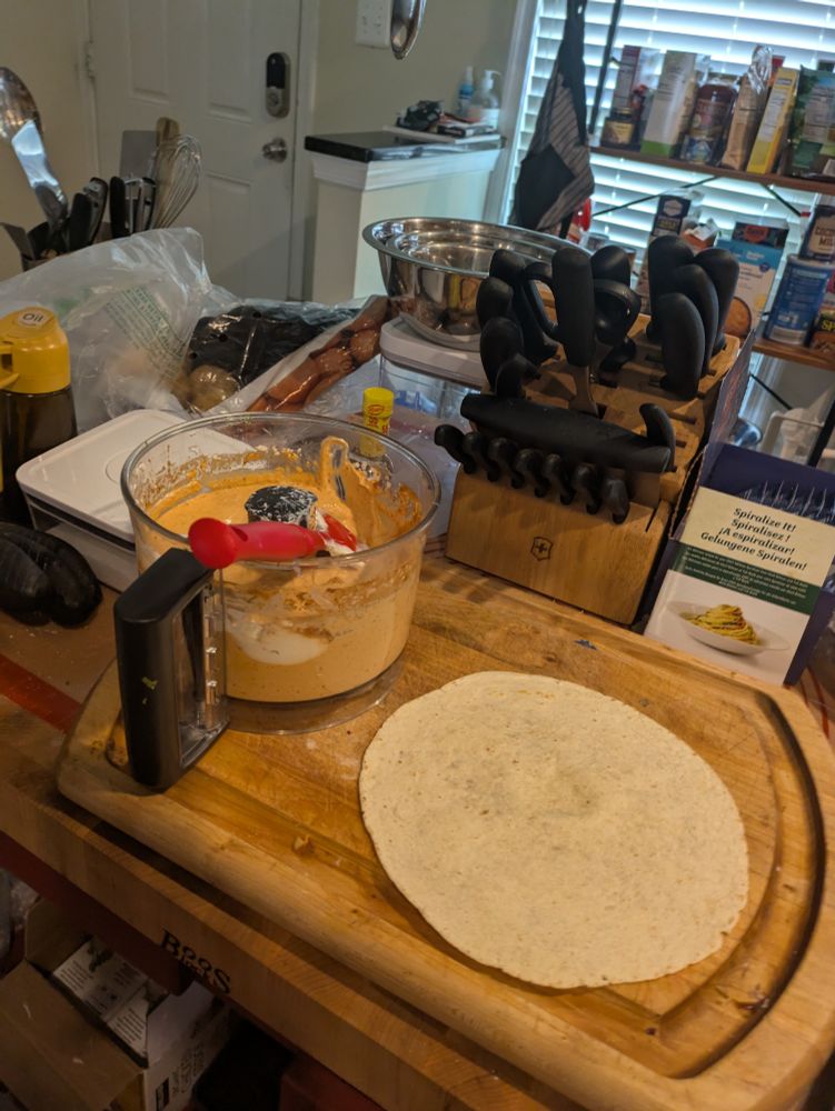 Burrito building station, warmed tortilla on cutting board with greek yogurt chipotle sauce in a food processor on the side. 