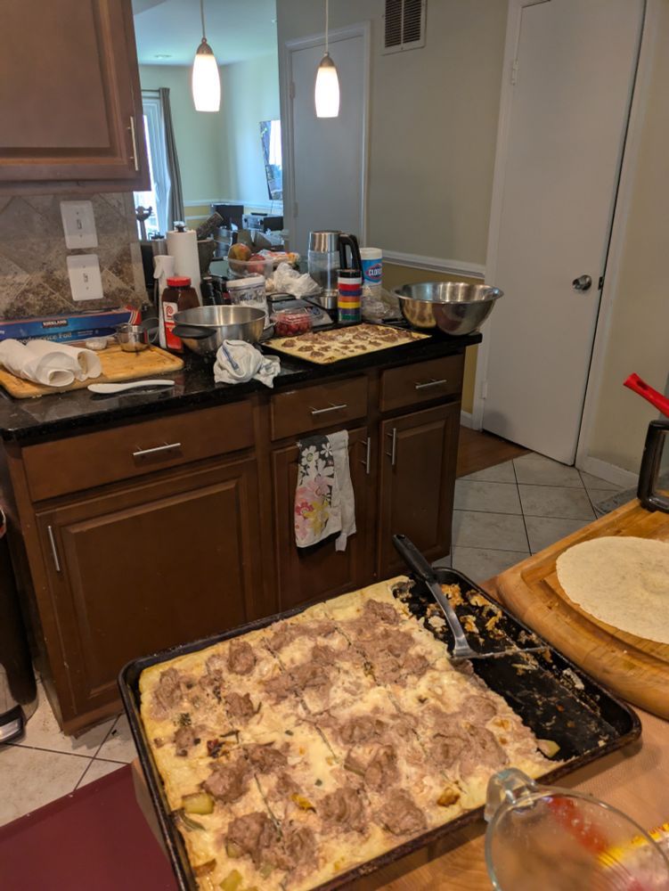 Sheet oan with some eggs scrapped out for burritos, other burritos wrapped in paper towels in the background with another sheetpan full of the cooked egg mixture. 