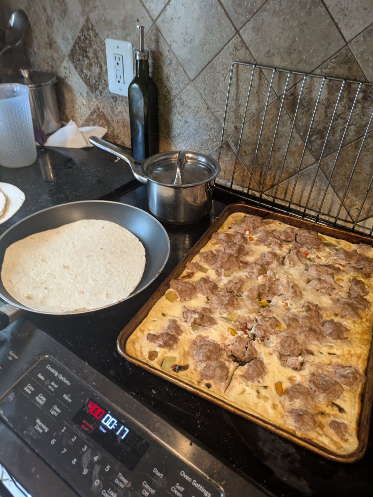 Sheet pan with egg, vegetable, and ground turkey mixture. A non-stick pan with a tortilla is on it. 