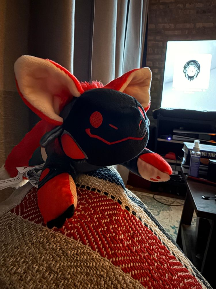 Stuffed weighted mini Protogen chilling on a pillow looking knowingly at the camera. Because it does, in fact, know. 