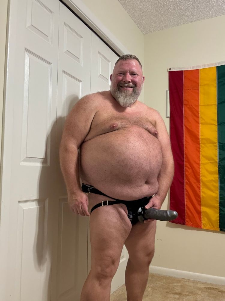 Bearded man proudly presenting his strap on with a big smile 