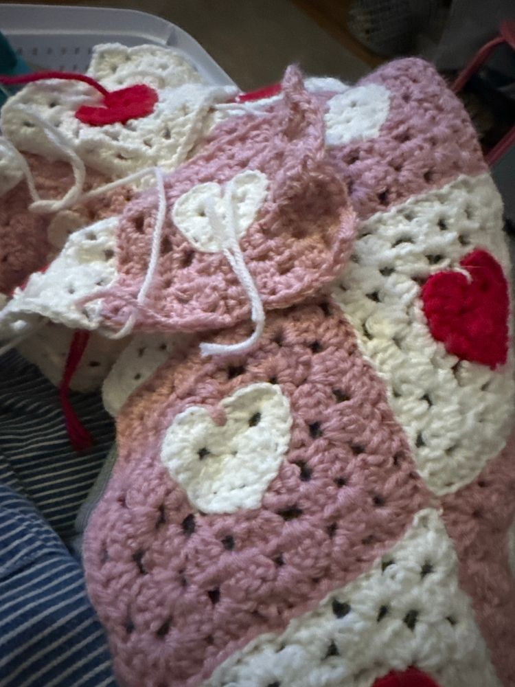 Crocheted granny squares with pink and white checks overlapped over someone’s lap