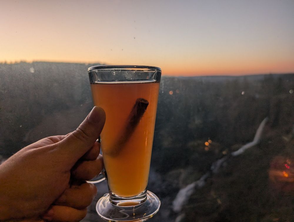 A glass of liqueur behind held overlooking a mountain range during a sunset