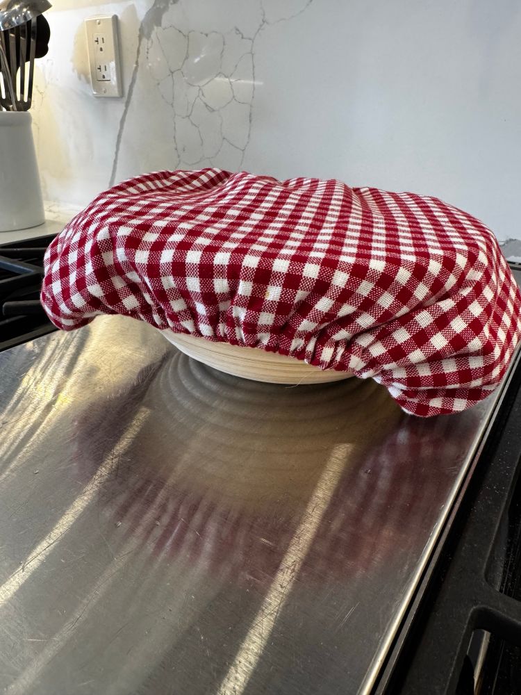 A banneton with a pretty red and white cover on it. There’s a boule under there. 