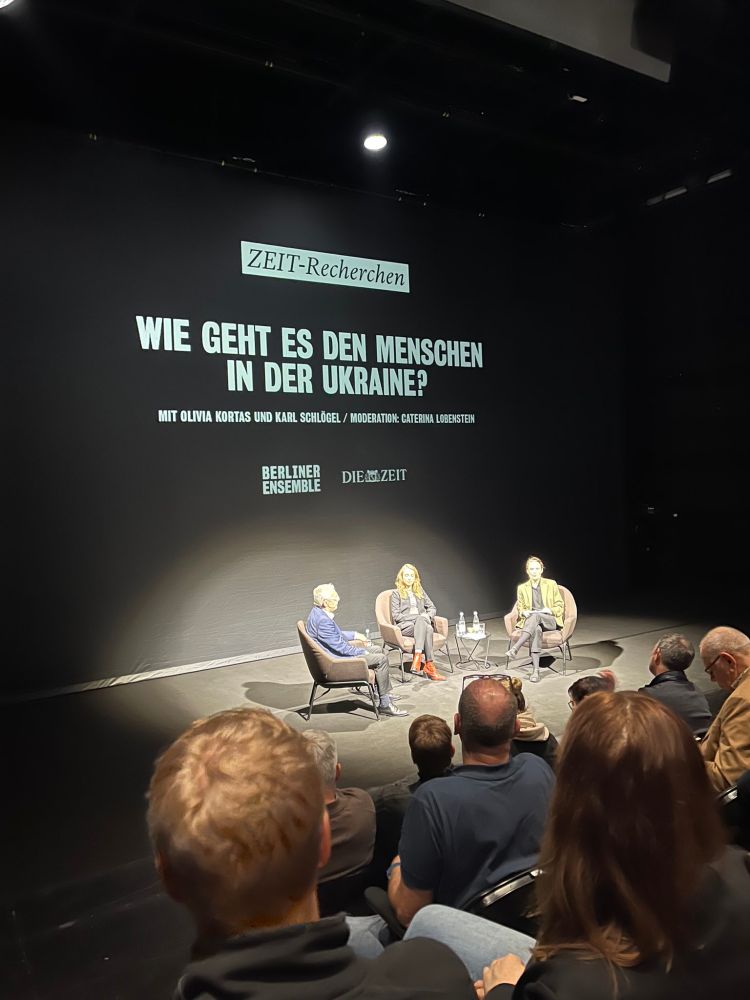 Drei Personen auf der Bühne, dahinter Projektion u.a. mit dem Text "Wie geht es den Menschen in der Ukraine" unter dem Titel Zeit-Recherchen