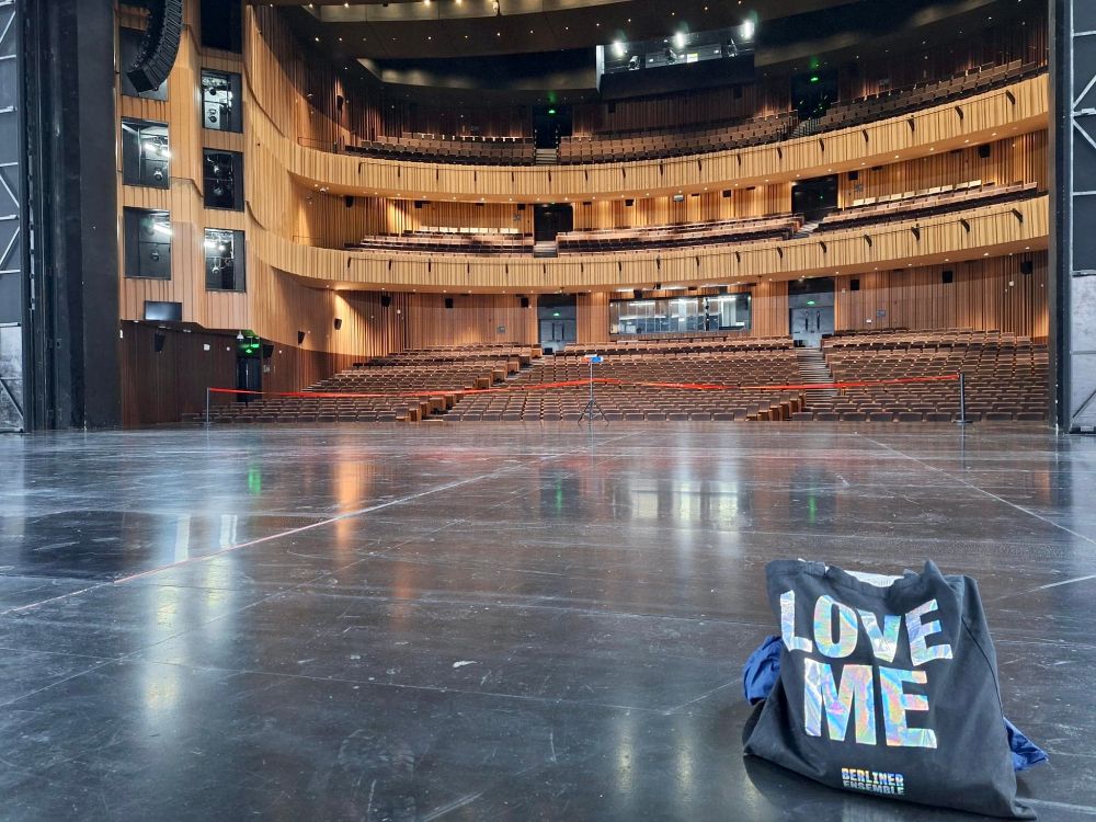BE-Stoffbeutel mit der Aufschrift "Love me" auf der leeren Bühne, im Hintergrund großer Zuschauerraum mit heller Holzvertäfelung