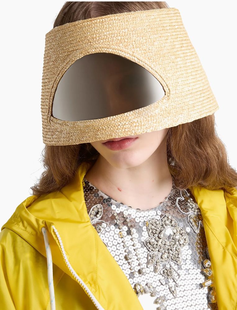 A woman wears a straw hat that covers her face. It has a plastic window in the front so she can see out, but her nose is also covered by the hat so you know that thing is all fogged up. 

Also, she’s wearing a sparkling silver top like she’s going clubbing, but she also has a bright yellow zip up hoodie over it for some reason.

The hat costs $2,800!