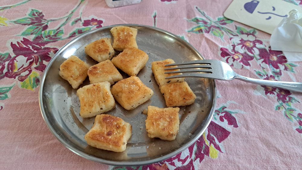 Square lightly browned gnocchi on a round metal plate; a fork rests on the right side of the plate 