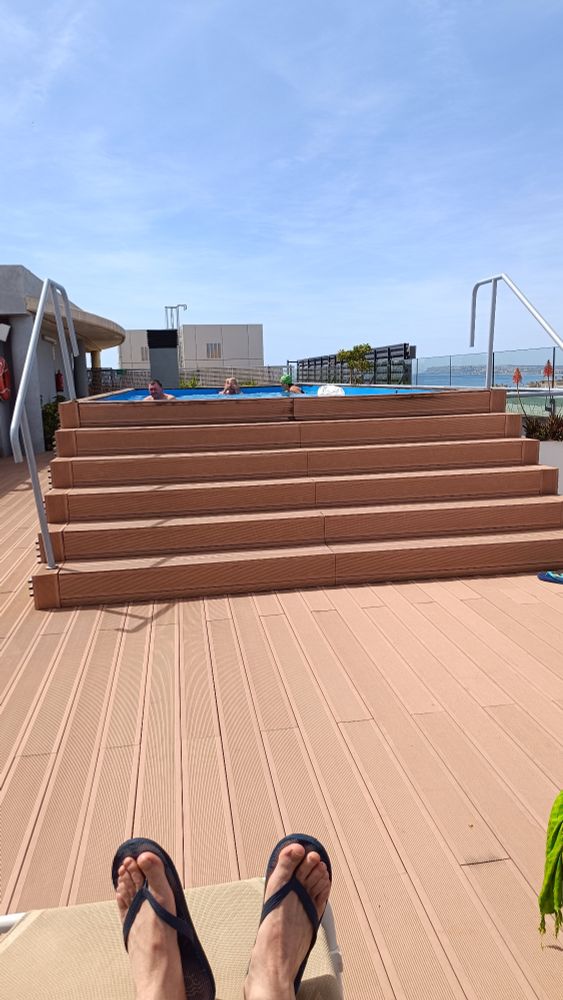 Rooftop swimming pool, sunny weather, blue skies. Feet in flip flops.