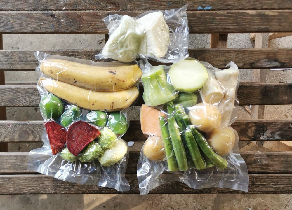 foto de um kit de legumes higienizados e embalados à vácuo contendo: batata inglesa, batata doce, banana da terra, quiabo, chuchu, beterraba, maxixe, jiló, abóbora maranhão e repolho. o kit está sobre um banco de madeira feito de pallets. 