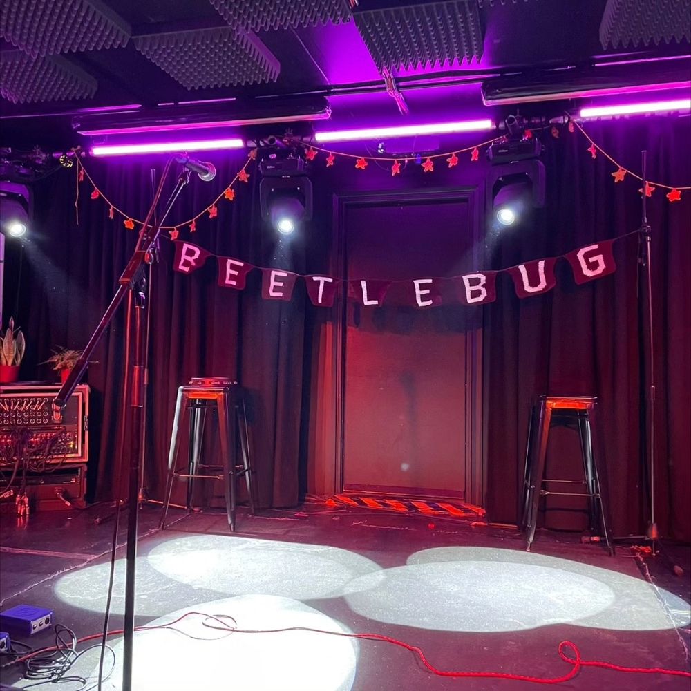 empty stage with a crocheted banner in red with white lettering that spells out "beetlebug"