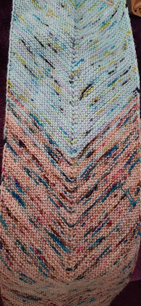 A chevron knitted patch where the base colour changes from beige with blue and pink speckles to a blue base with pink and green speckles