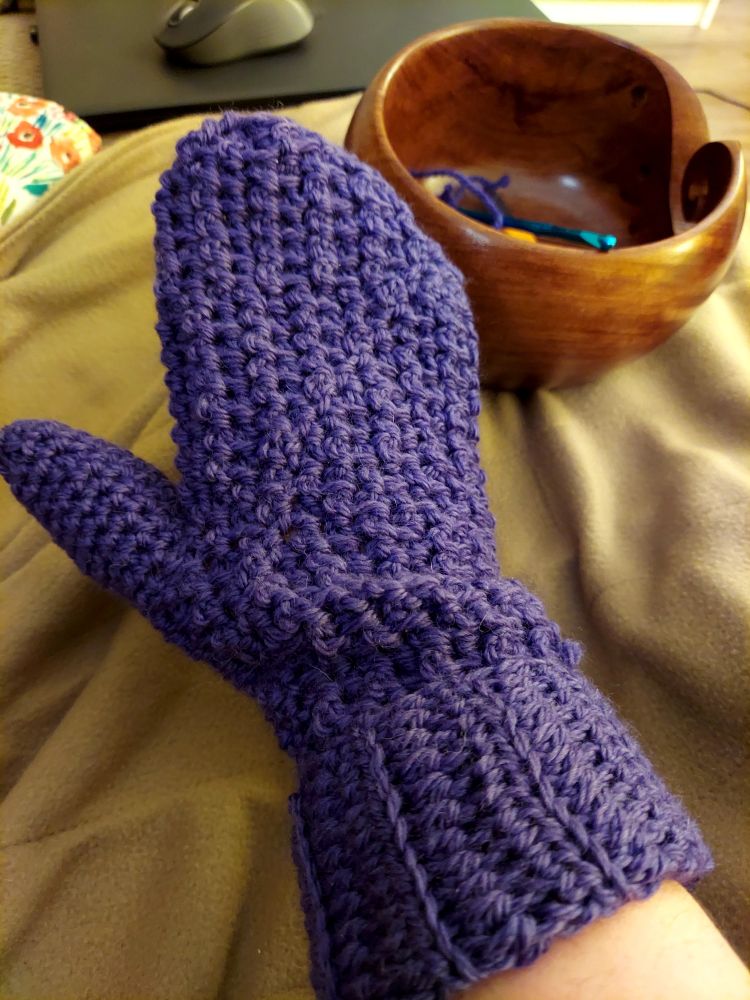 A picture of the backside of a completed crochet mitten in purple wool yarn.