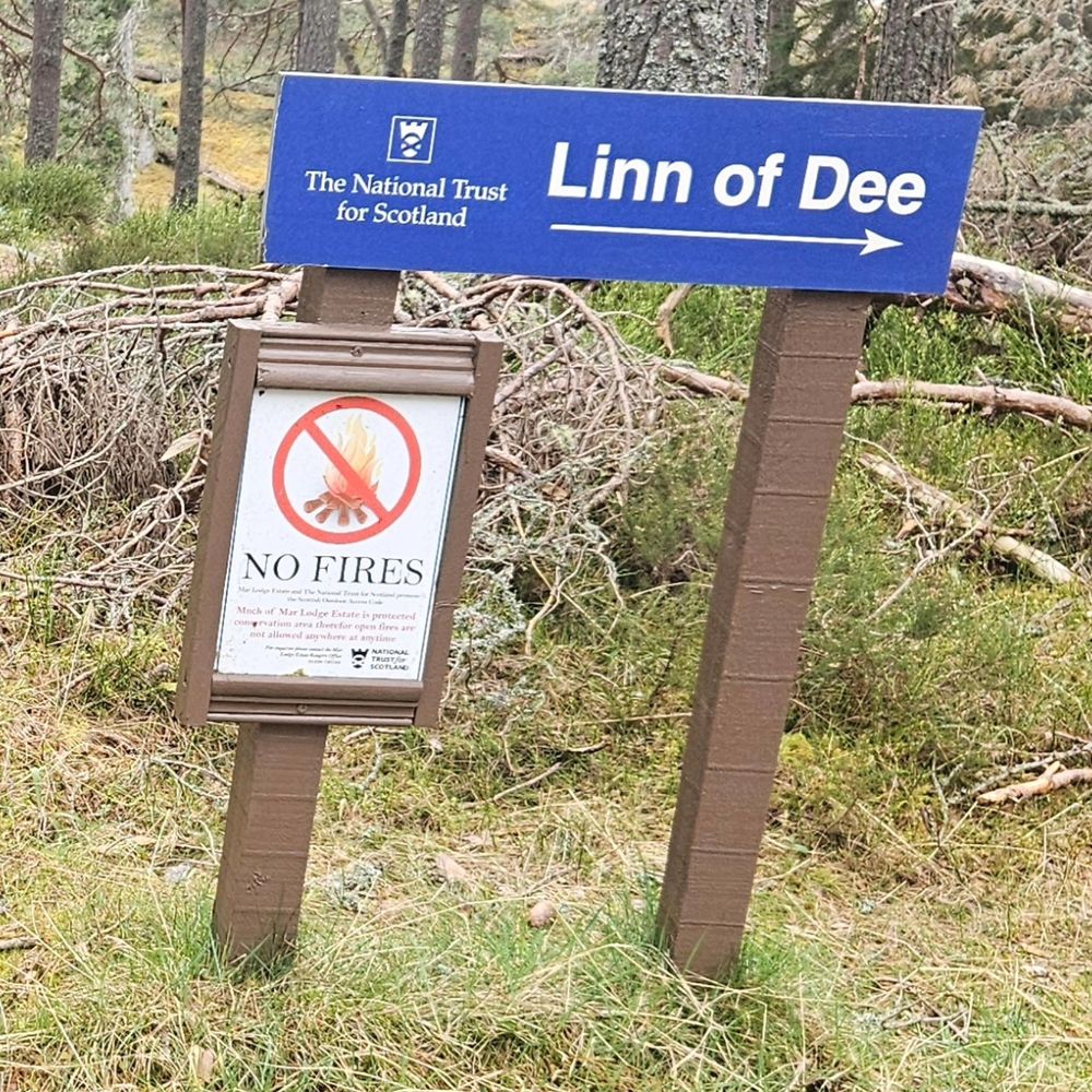 A National Trust sign for the Linn of Dee. A second sign, attached to the post and okay a picture frame, reads NO FIRES, with a picture of a campfire with a red line through it.
