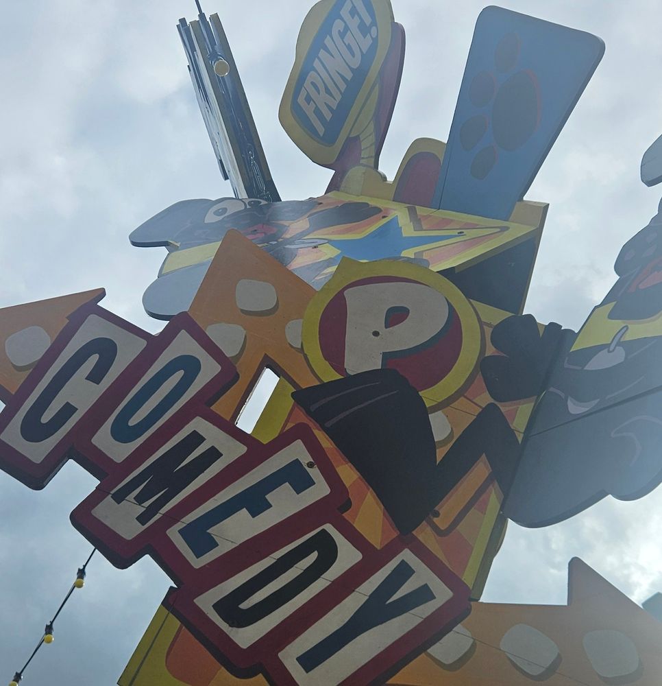 A colourful sign in Pleasance Courtyard with various arrows pointing in different directions. "Fringe" and "Comedy" signs are visible
