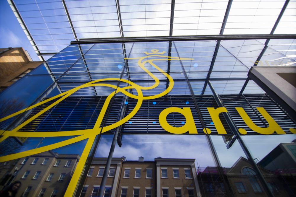 Image of the front of Helmore building on our Cambridge campus.
A blue glass building with a yellow heron logo and 'a.r.u.'. Reflection of the street opposite in the glass.