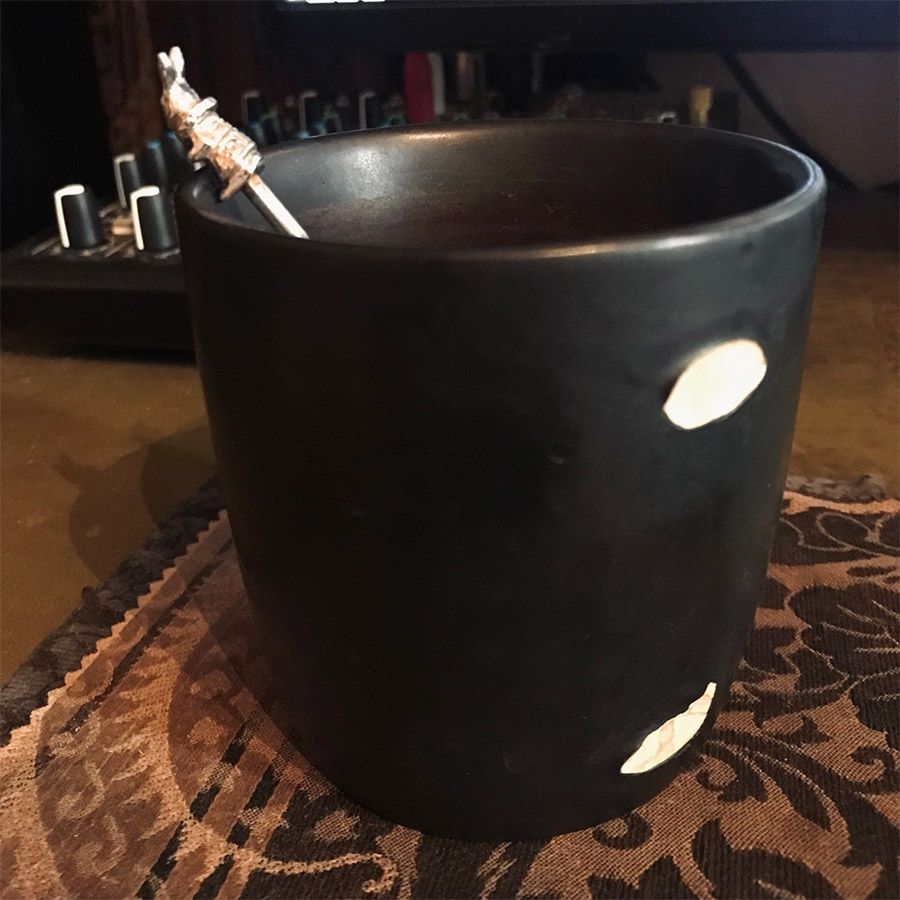 A simple black mug with a silver teaspoon in the shape of the white rabbit from Alice in Wonderland. The mug's handle is broken. 