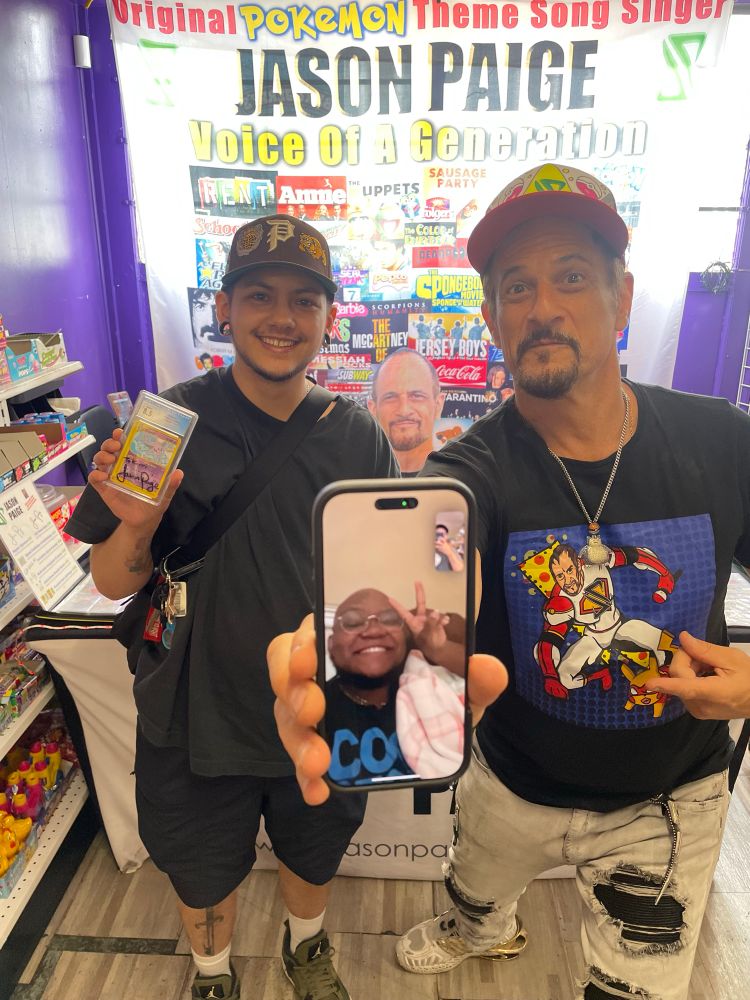 korri standing with jason paige. korri is holding a CGC graded Aquapolis Espeon card signed by jason. jason is holding korri’s phone which has his friend Sketch on facetime so he could also meet jason.
