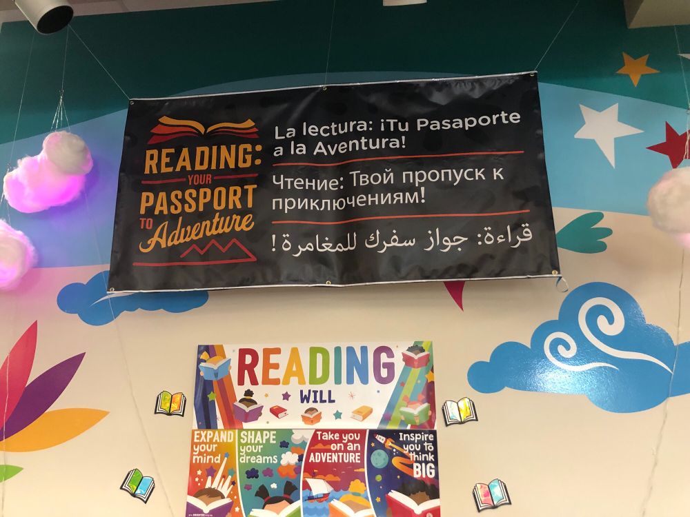 Poster that says Reading Your Passport to Adventure in English, Spanish, Russian and Arabic.