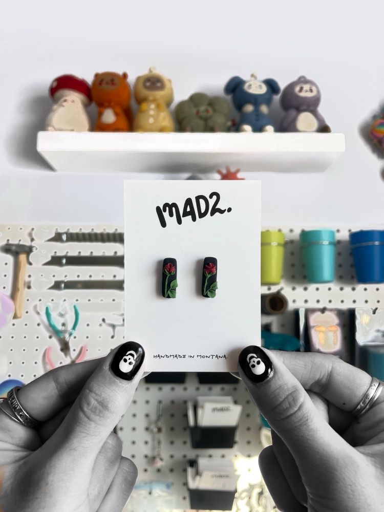 Holding tiny rose stud earrings in front of my pegboard wall 