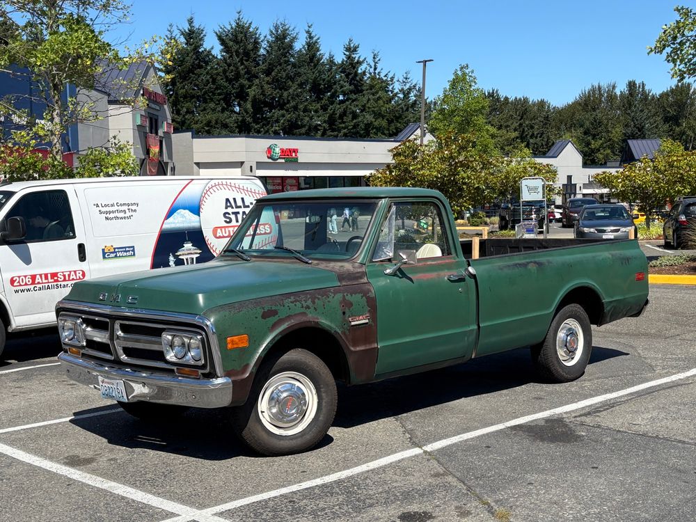 Picture of an old green GMC pickup in a parking lot 