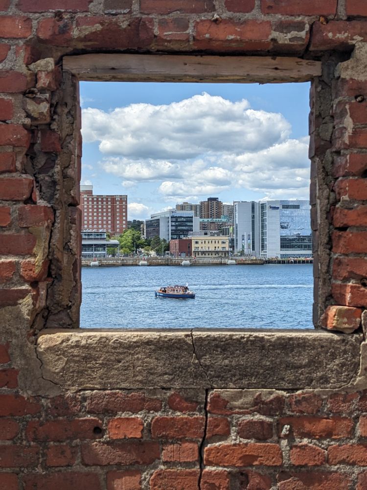 A view of the Halifax waterfront seen through the square frame of a brick wall on Georges Island