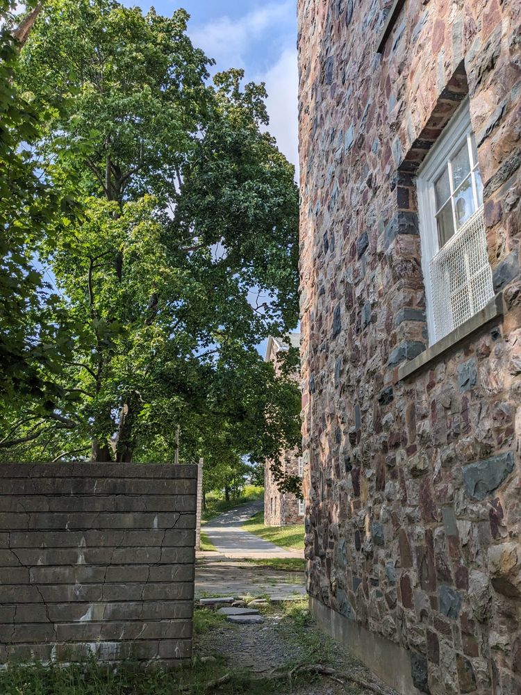 A shortcut. I wonder if you know where it is? A stone building and a wooden wall looking through to a shady path
