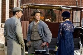 Miss Fisher in a blue lace dress stands in front of a vintage car with Bert and Cec
Still from Miss Fisher's Murder Mysteries 