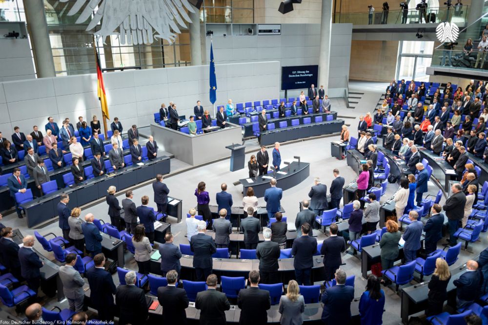 Zu sehen ist der Plenarsaal des Deutschen Bundestages. Die Abgeordneten haben sich zu einer Schweigeminute für die Opfer des Terrors in Israel erhoben.