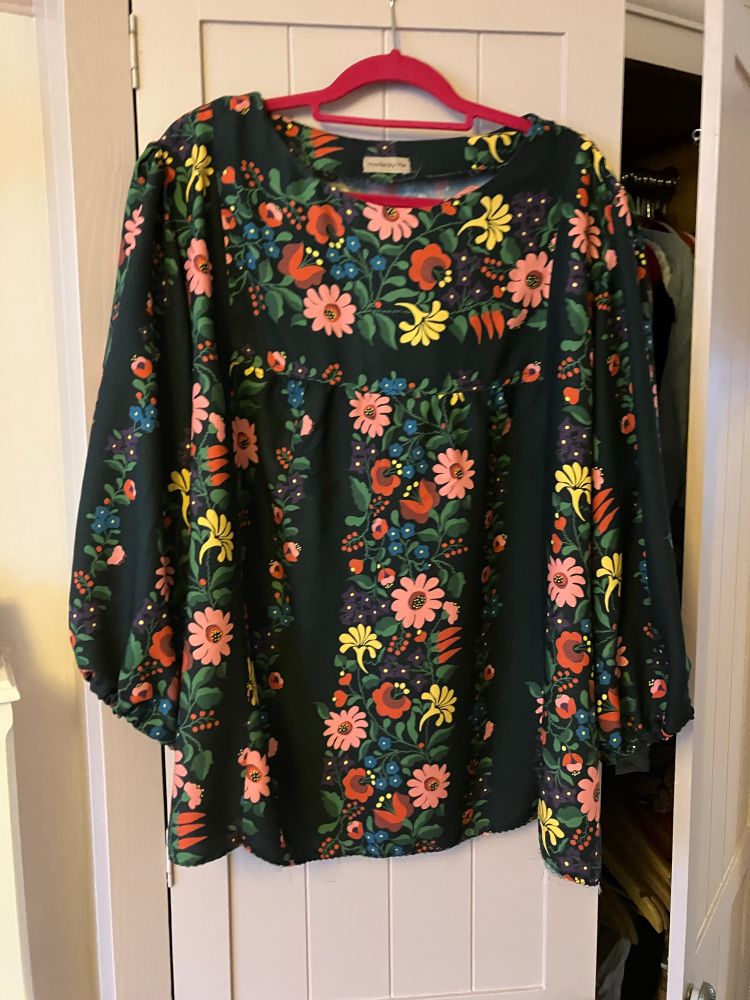 A smock blouse in a patterned fabric. A vibrant floral motif on a black background 