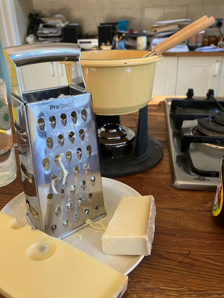A cheese grater, two blocks of cheese and a fondue set.