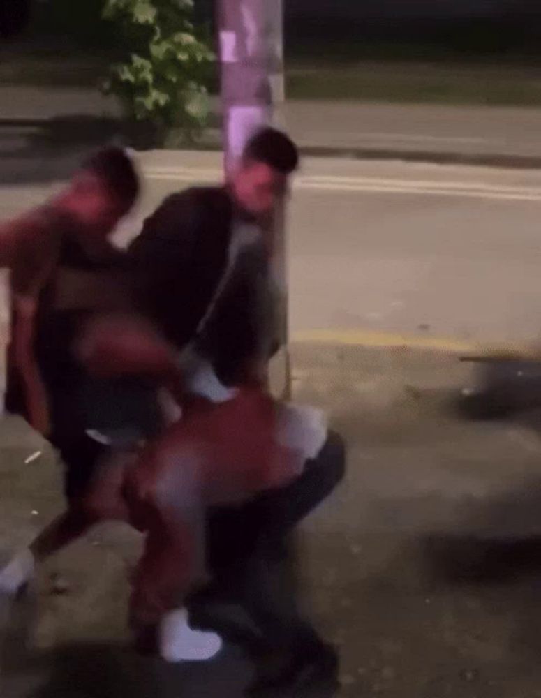 a blurry photo of a group of people fighting on the sidewalk