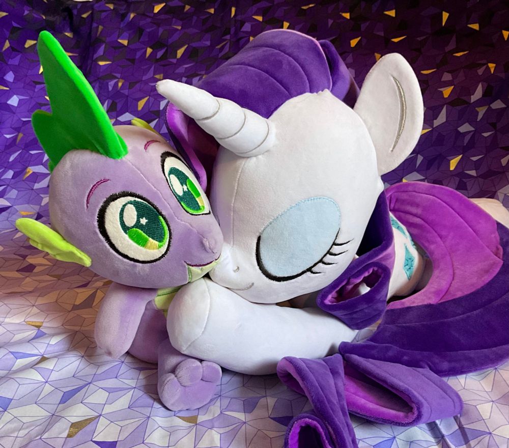 A photo of a handmade 20-inch plush doll of Rarity from My Little Pony: Friendship is Magic in a laying pose with a relaxed, sleeping expression against a purple backdrop hugging another handmade doll of her good friend, Spike the Dragon.