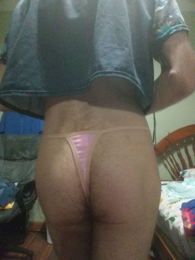 A view of my ass wearing a blue dino explorer crop top, and a cute pink thong. Bedroom in the background, chair on left, bed on right with dino bedsheets.