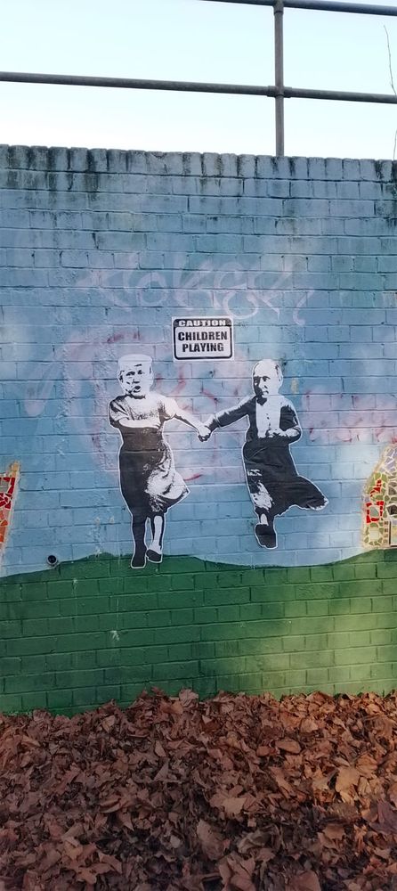 Wall art depicting Trump and Putin as children under a sign saying Caution Children Playing