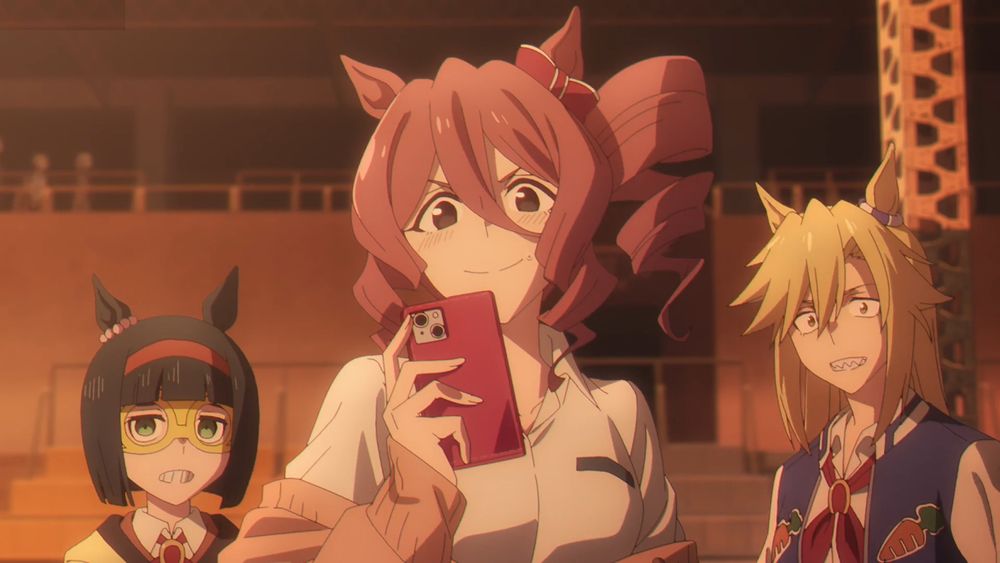 Norn Ace (in front of the audience seating) gives a big smile while blushing and holding up her phone camera; Rudy and Mini look a little awkward behind her