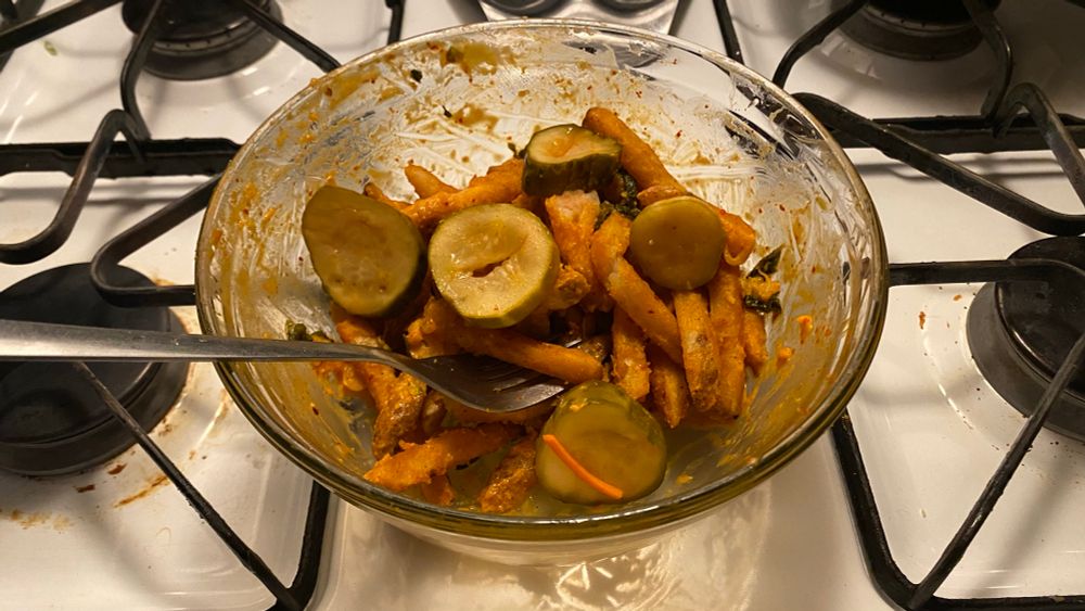 A slightly eaten bowl of kimcheese fries topped kimchi pickles