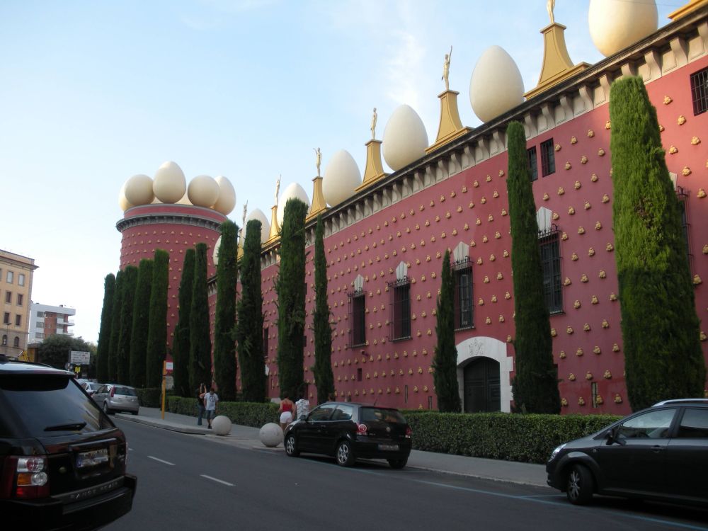 A building with a pink facade with gold adornments and what appear to be large eggs on the upper exterior 