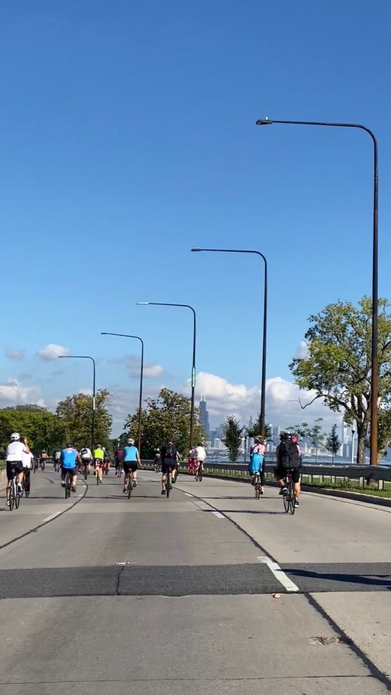 Northward view of Chicago from lake shore drive. There are cyclists on the road and you can see the sears / Willis tower in the skyline