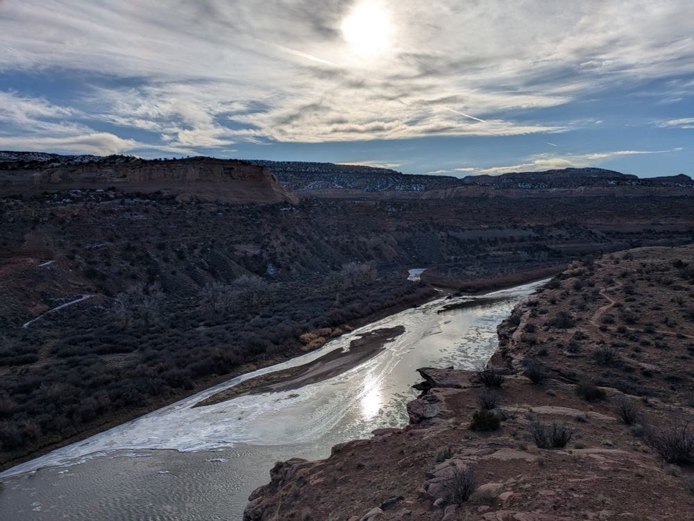Parts of the Colorado river have ice on them. Clouds and a little bit of blue sky above the canyon 