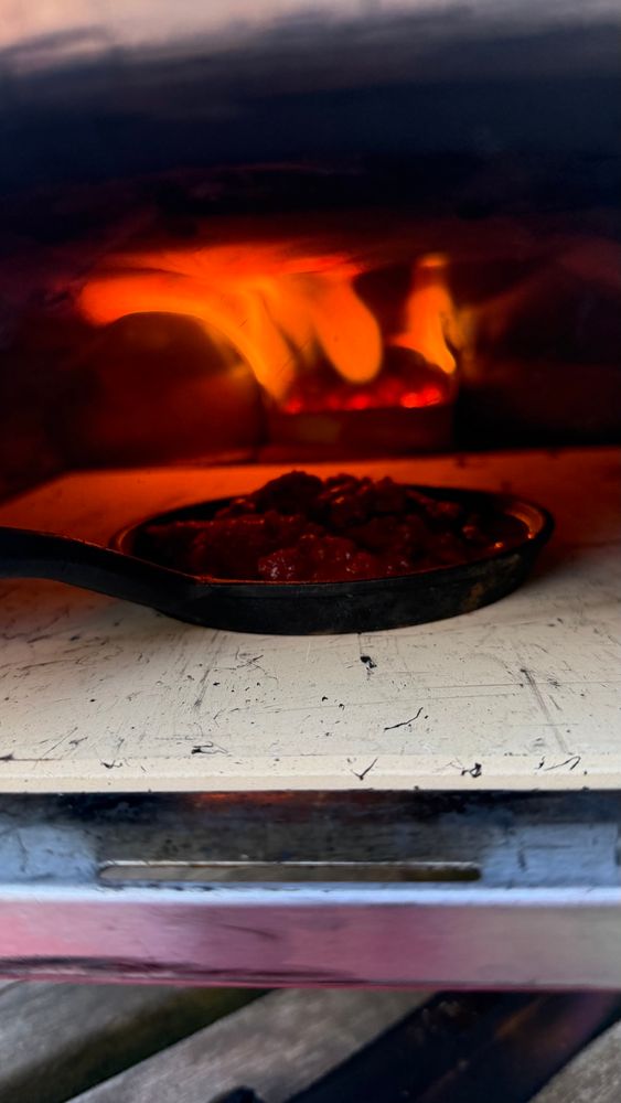 A small pan with pasta sauce heating up in the oven with flames rolling over it. 