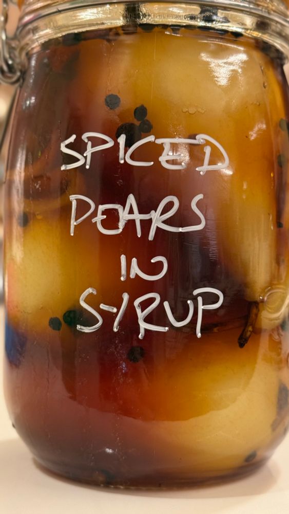 Pears in a preserving jar, with “Spiced Pears in Syrup” written on the side in white marker pen. 