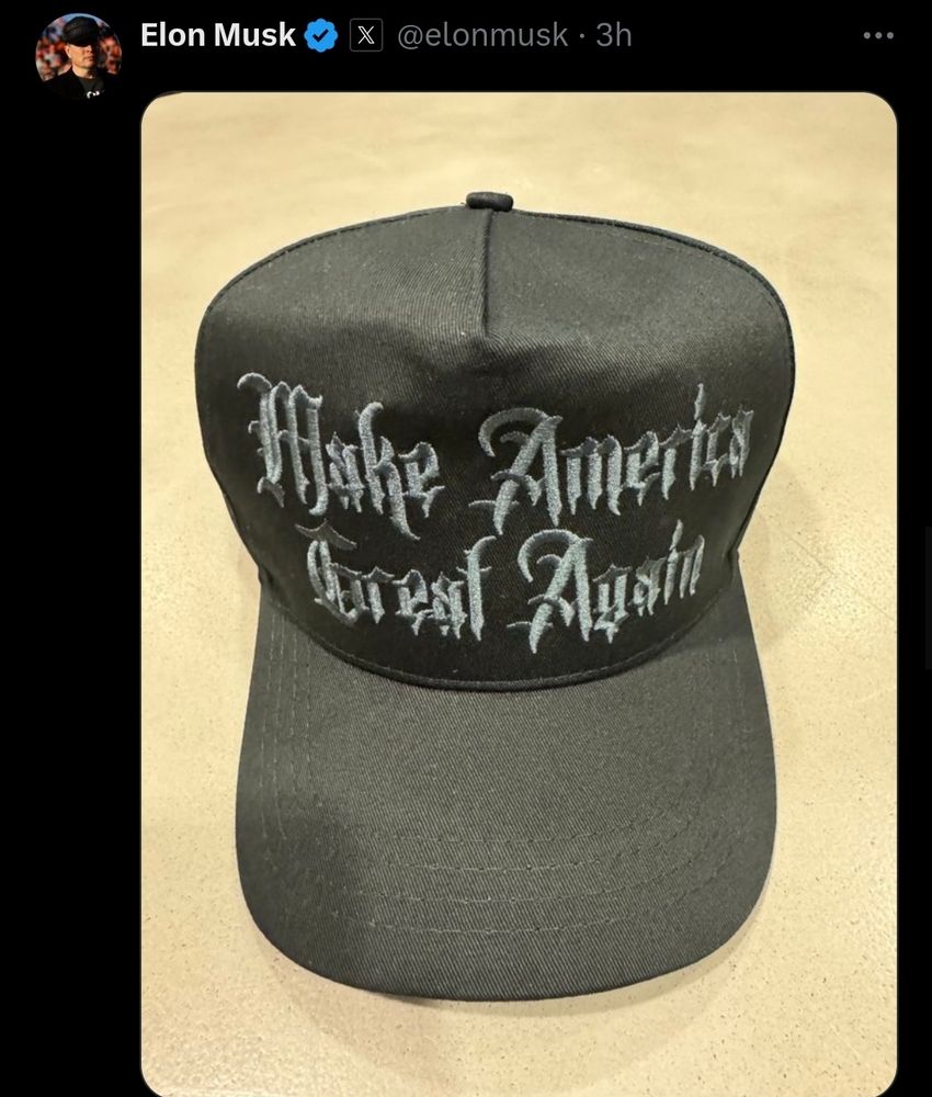 The image shows a black baseball cap with the phrase "Make America Great Again" embroidered in a gothic-style, white font. The tweet is from Elon Musk's verified Twitter account, and the tweet was posted 3 hours ago. The cap is placed on a light-colored surface, and the focus of the image is on the cap and its embroidered text.

