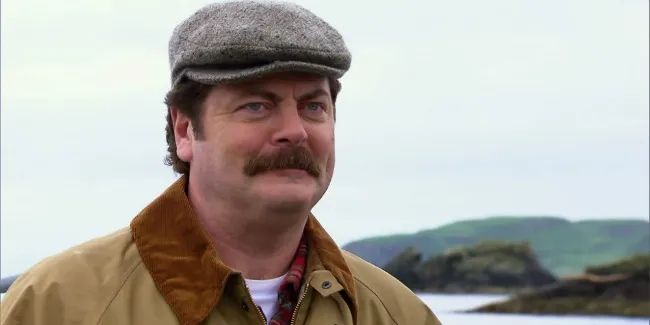 Ron Swanson dressed in a hat and jacket, standing outside and looking towards and past the camera with a happy, satisfied expression on his face.
