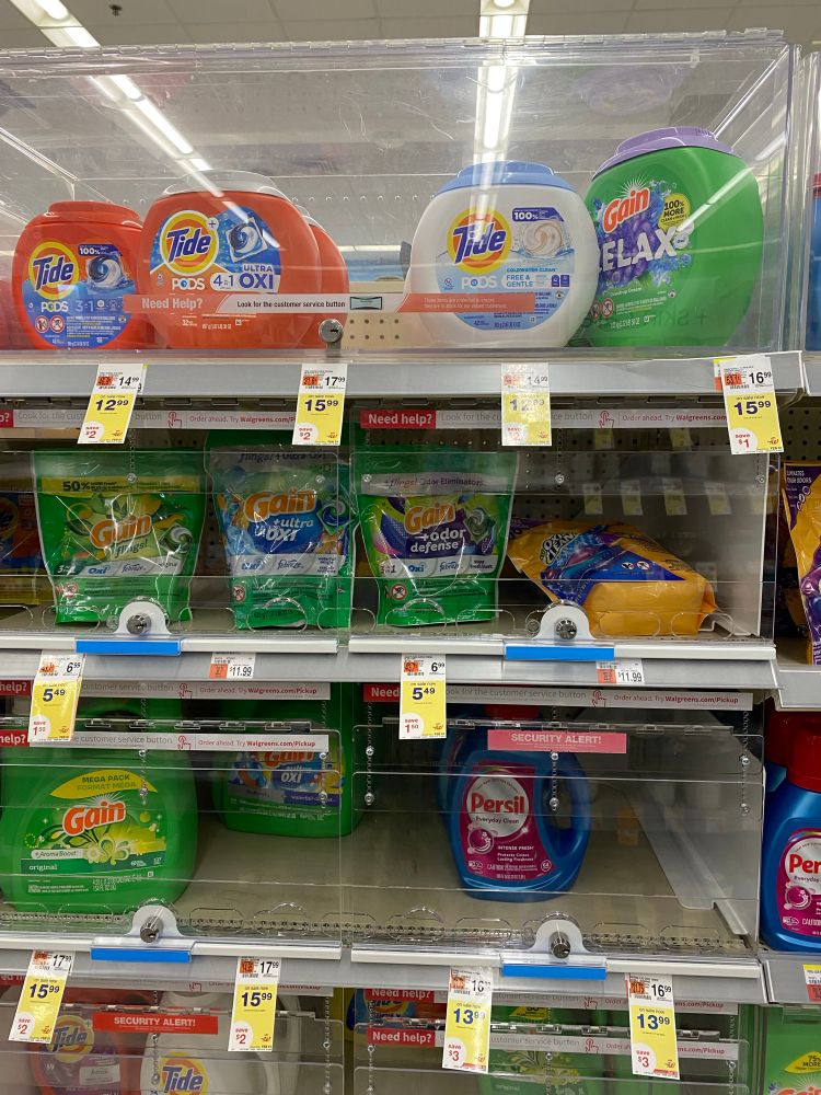 A variety of laundry detergents on store shelves behind locked cases.