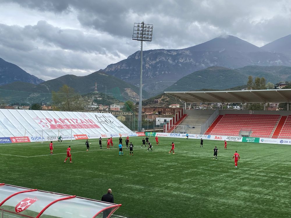 Stadion Partizani in Tirana, ein Teil der Tribüne, ein Flutlichtmast, und ein Gebirge sind im Hintergrund zu sehen, im Vordergrund sieht man die Spieler und das Spielfeld 