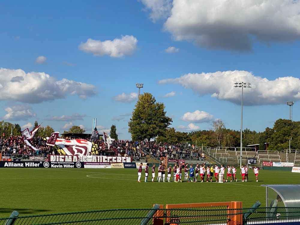 Spielfeld beim Auflaufen der Mannschaften, im Hintergrund der Fanblock des BFC Dynamo mit einer Blockfahne